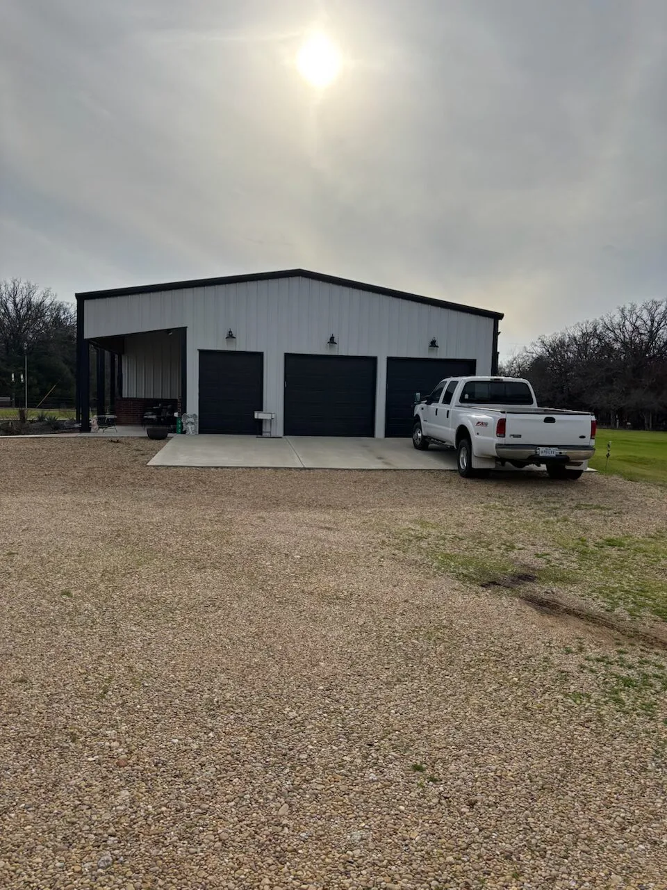 white pickup truck parked next to a black garage door attached to a white barndominium