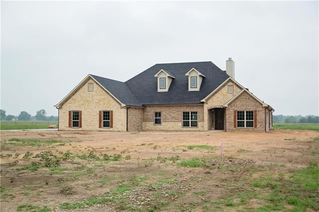 Large single-story brick home with dark shingle roof, dormer windows, and spacious rural lot under an overcast sky.