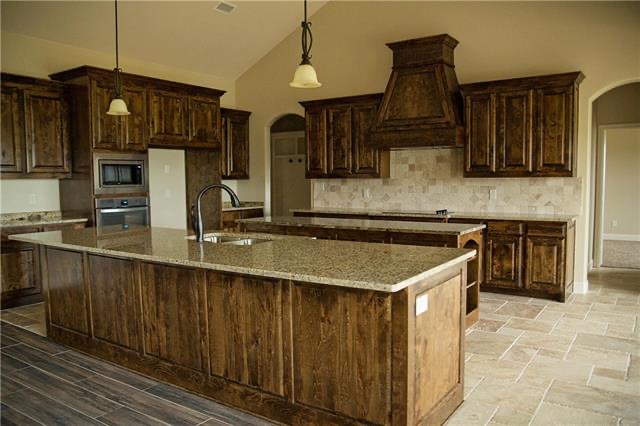 Finished barndominium kitchen with rustic wood cabinetry, large island, granite countertops, and tile flooring for a Chattanooga home.
