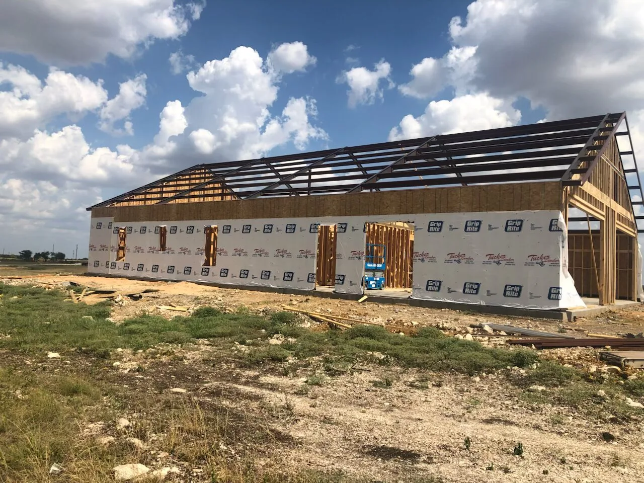 Barndominium shell under construction with house wrap, wood framing, and metal roof structure on a Chattanooga-area building site.